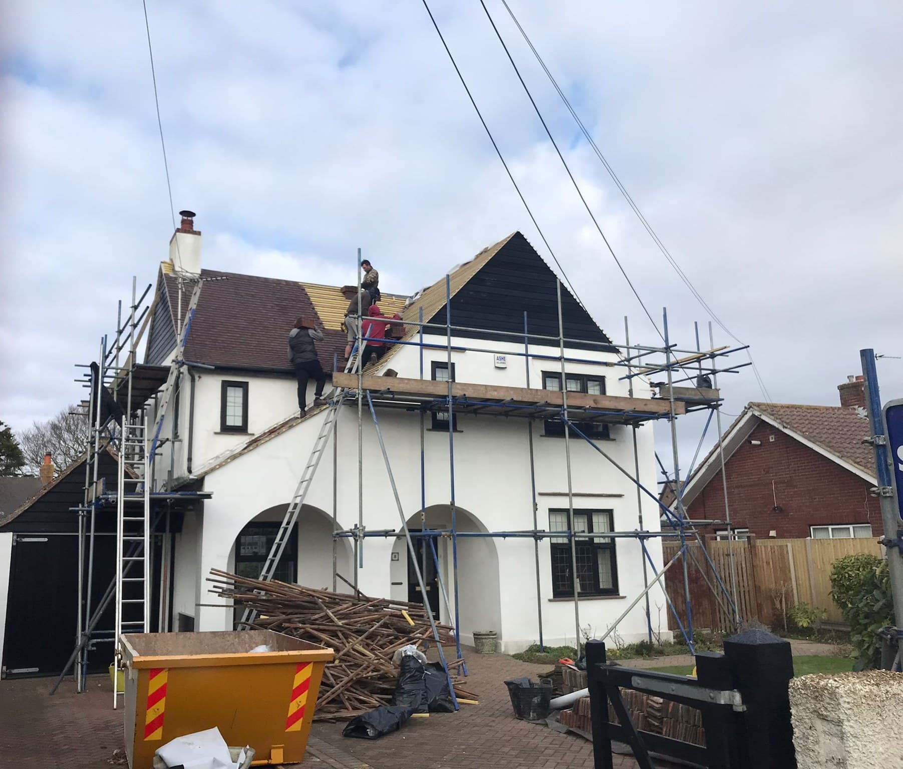 Roofers working on a scaffolded house in Hythe under a blue sky